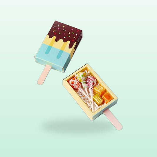 Blue ice lolly party favour boxes with a chocolate drip top, one slid open showing sweets, on a mint background