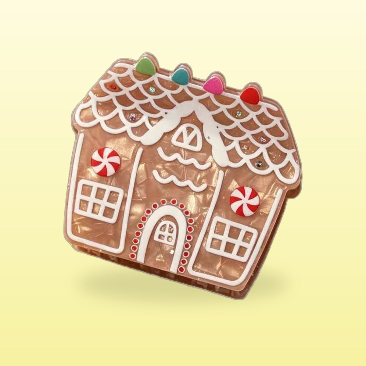 Classic gingerbread house claw clip with white icing, gumdrops and peppermint swirls on a butter yellow background