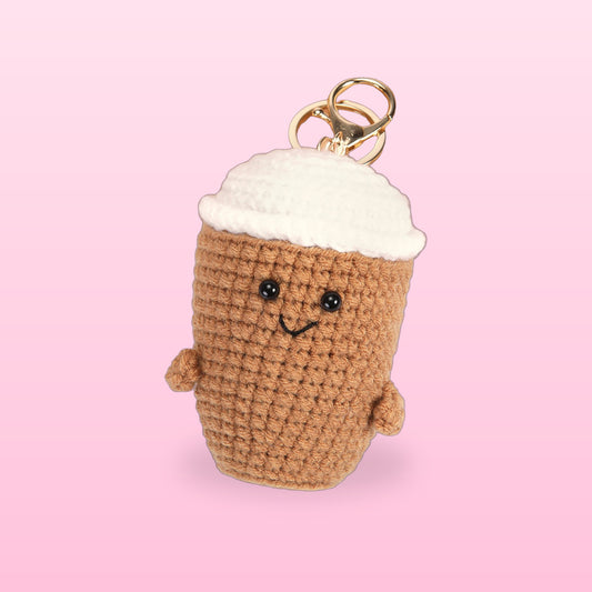 Latte crochet coffee cup bag charm with a white lid, bead eyes and a stitched smile on a soft pink background