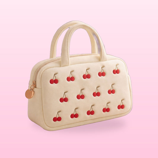 Cream cherry embroidered vanity bag with twin handles on a pink background