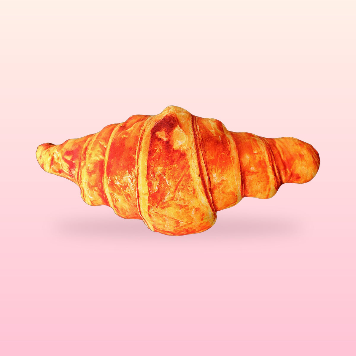 Giant croissant hug pillow with a golden flaky bakery print on a soft pink background