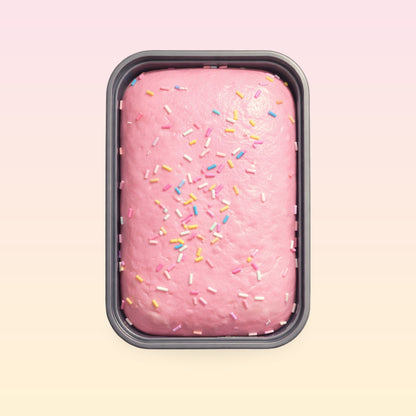 Pink strawberry sprinkle cake squishy in its grey tray on a pink and cream background