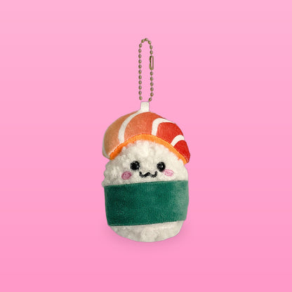Salmon sushi plush keychain with a green nori band, bead eyes and rosy cheeks on a soft pink background