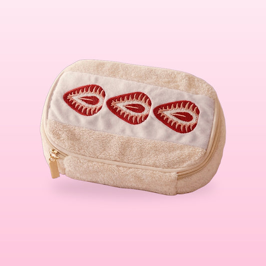 Strawberry Sando Makeup Bag in fluffy cream plush with three embroidered strawberry halves on a pink background