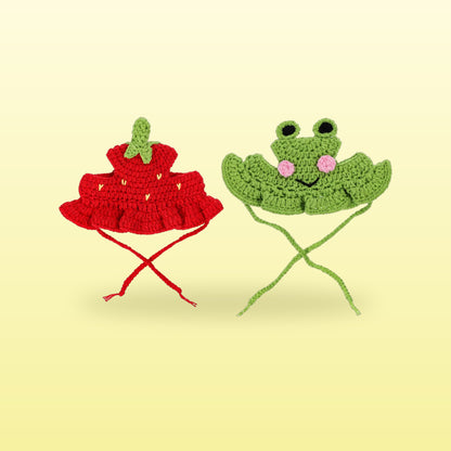 Red strawberry and green frog crochet cat hats with tie strings on a butter yellow background