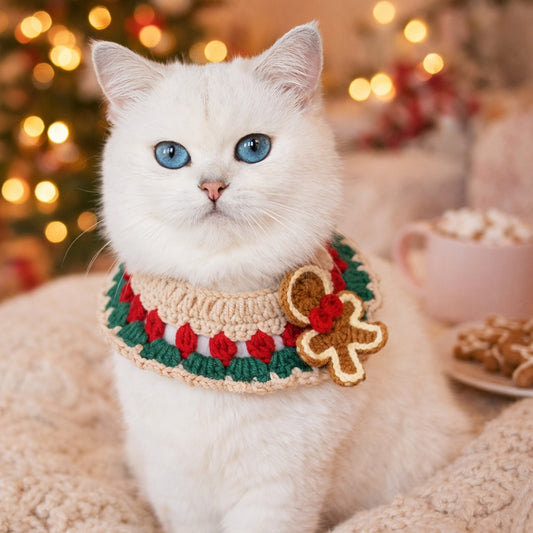 White cat wearing the gingerbread crochet collar by a Christmas tree with gingerbread biscuits