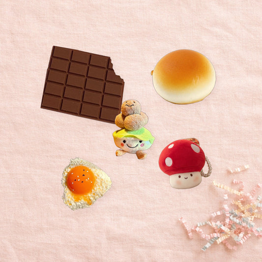 Example lucky bag of five snacks on pink linen: memo pad, bun squishy, dim sum charm, egg squishy, mushroom charm