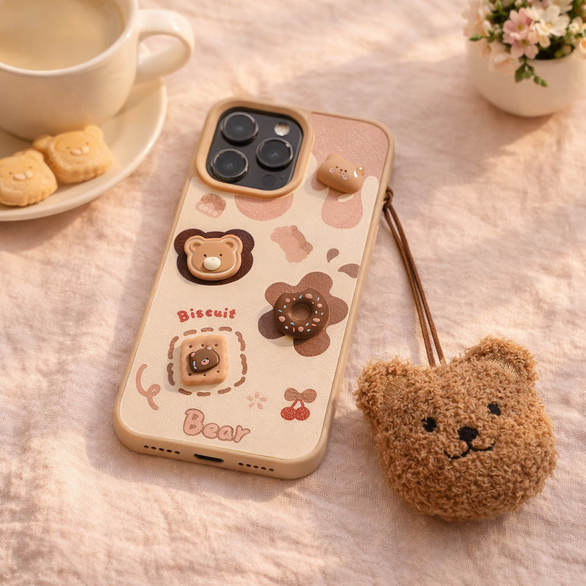 Biscuit bear iPhone case and plush bear charm on a pink linen cloth beside a cup of milky coffee and bear biscuits