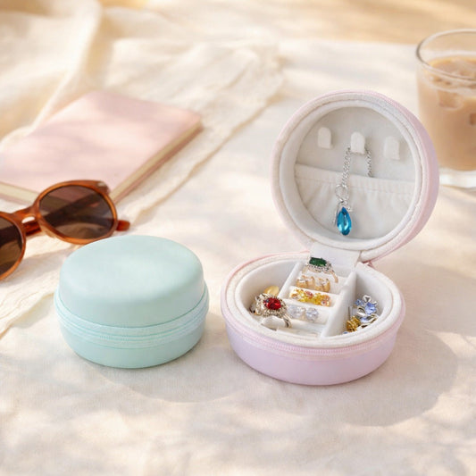 Mint and rose macaron jewellery cases on a sunny hotel table beside sunglasses, one open with rings and a necklace inside