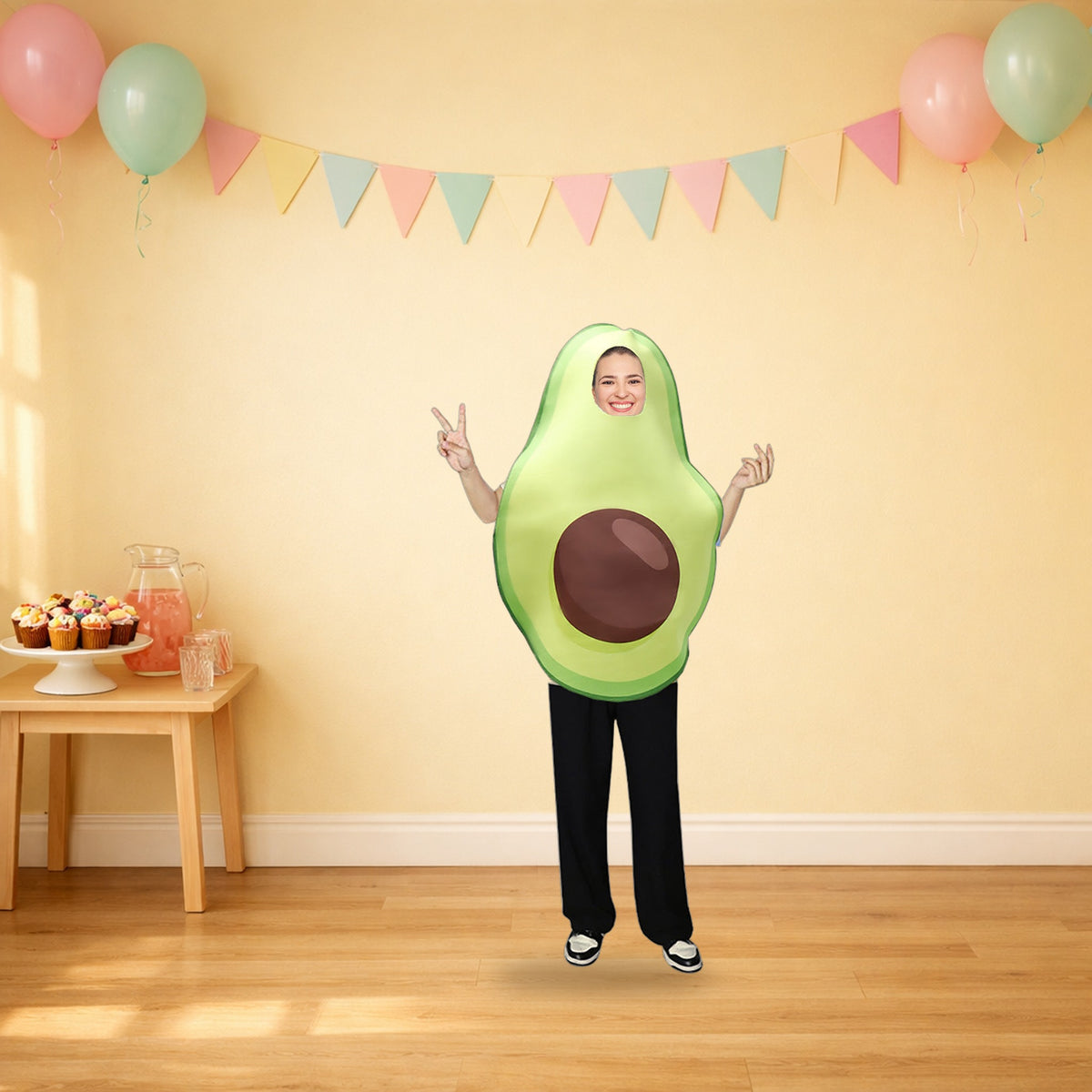 An adult in the avocado food costume at a pastel party with balloons, bunting and cupcakes