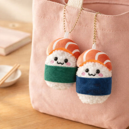 Green and blue salmon sushi plush charms hanging from a pink tote bag on an oak table