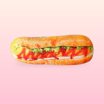 Hot dog hug pillow with a sesame bun, sausage, cheese, lettuce and ketchup print on a soft pink background