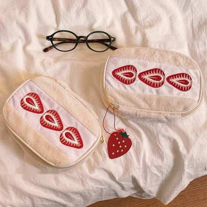 Two strawberry sando makeup bags, the set of 2 option, on soft white bedding