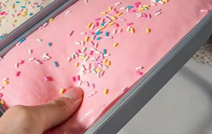 Thumb pressing into the pink strawberry cake squishy in its tray to show the soft squish and size