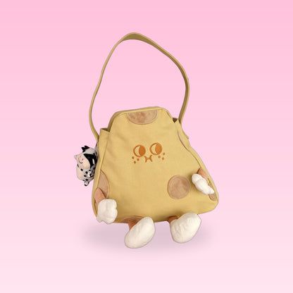 Cheese tote bag with a shoulder strap, plush legs and a cow charm on a pink background