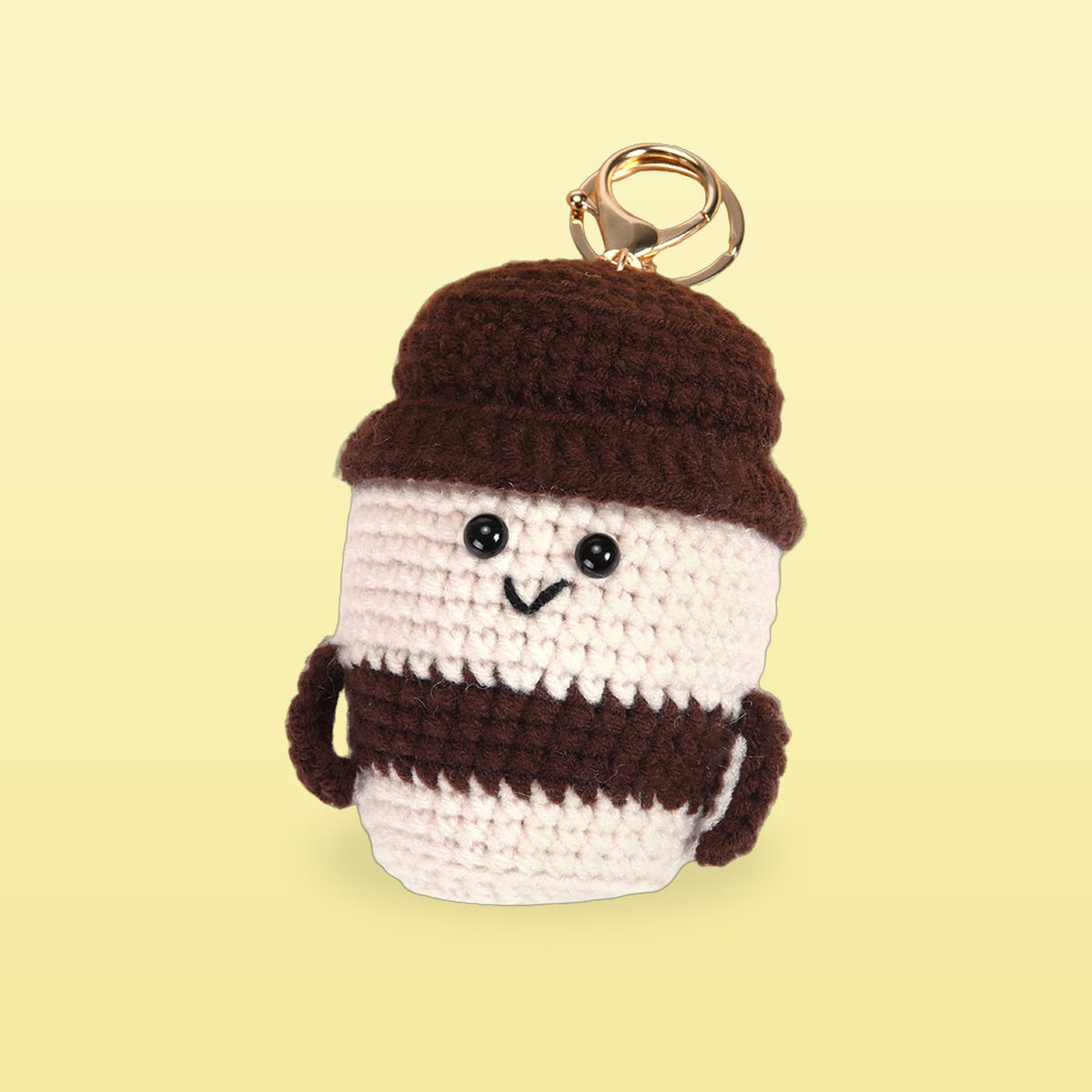 Mocha crochet coffee cup bag charm with a chocolate brown lid and band on a butter yellow background