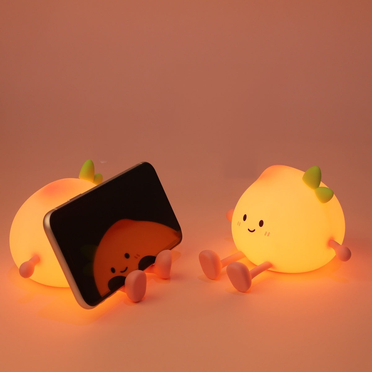 Two peach night lights glowing, one with a phone resting against it to show its size