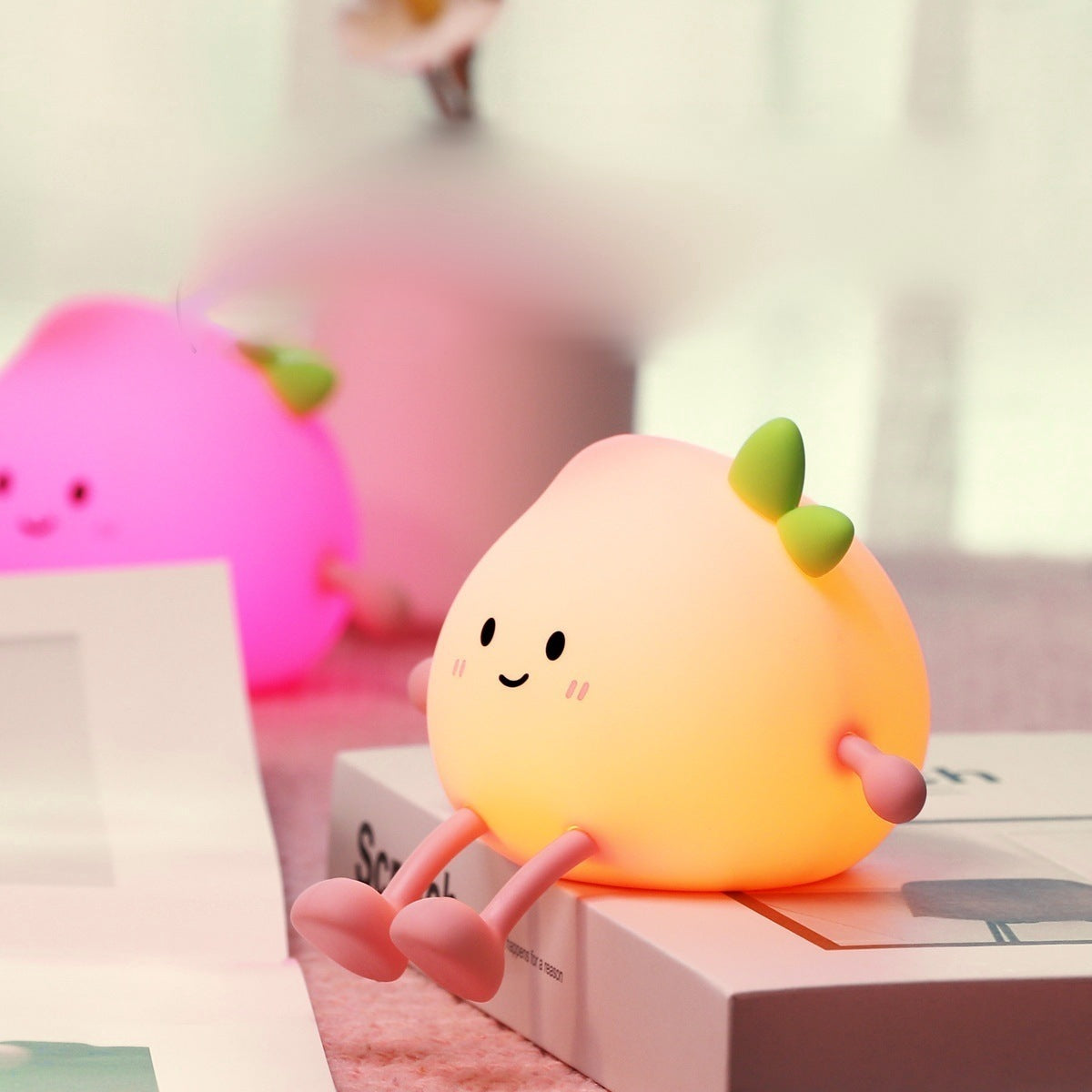 Multicolour peach night light glowing hot pink behind a warm glowing peach on a book