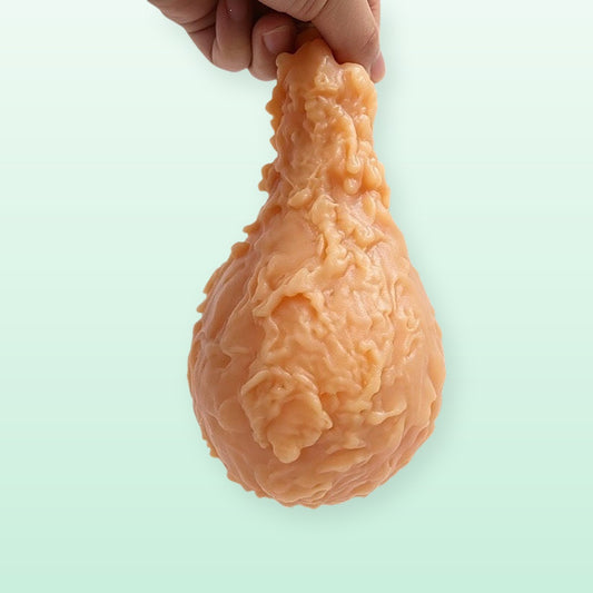 Jumbo fried chicken drumstick squishy held up by the bone end on a soft mint background