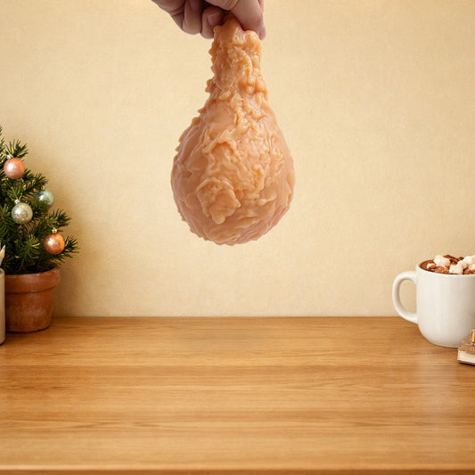 Fried chicken drumstick squishy dangling above a wooden desk with a mini Christmas tree and a mug of hot chocolate