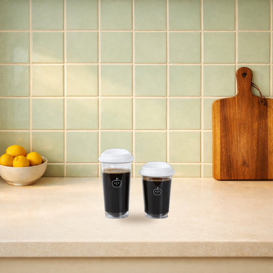 Two apple face glass cups with white lids on a kitchen bench beside a bowl of lemons