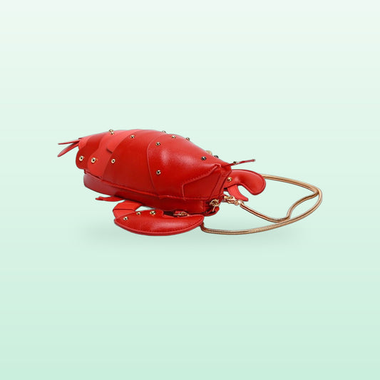 Red lobster crossbody bag with gold studs and a gold snake chain strap on a mint background
