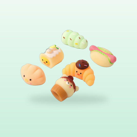 Mini bakery squishies including a croissant, hot dog, cake roll, bun and bear cupcake, on a mint background