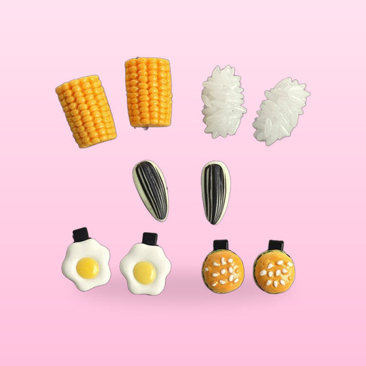 Food hair clip pairs: corn, rice, sunflower seed, fried egg and burger bun on a pink background