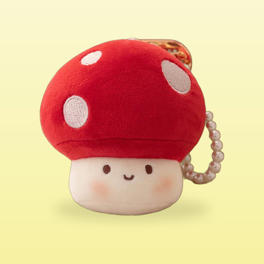 Red mushroom plush keychain with white spots and a pearl chain, on a butter yellow background