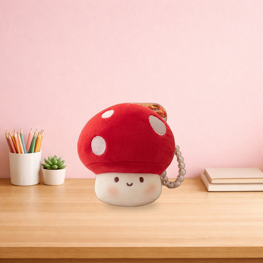 Red mushroom plush keychain sitting on a light oak desk beside a pot of pencils