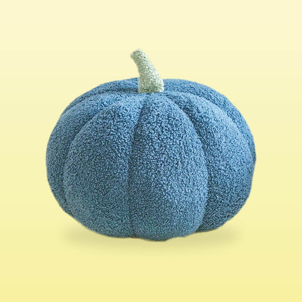 Teddy pumpkin plush cushion, denim blue with a sage stem, on a butter yellow background