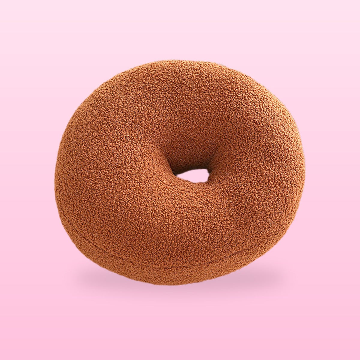 Sweet donut cushion in warm brown boucle with a centre hole, on a bubblegum pink background