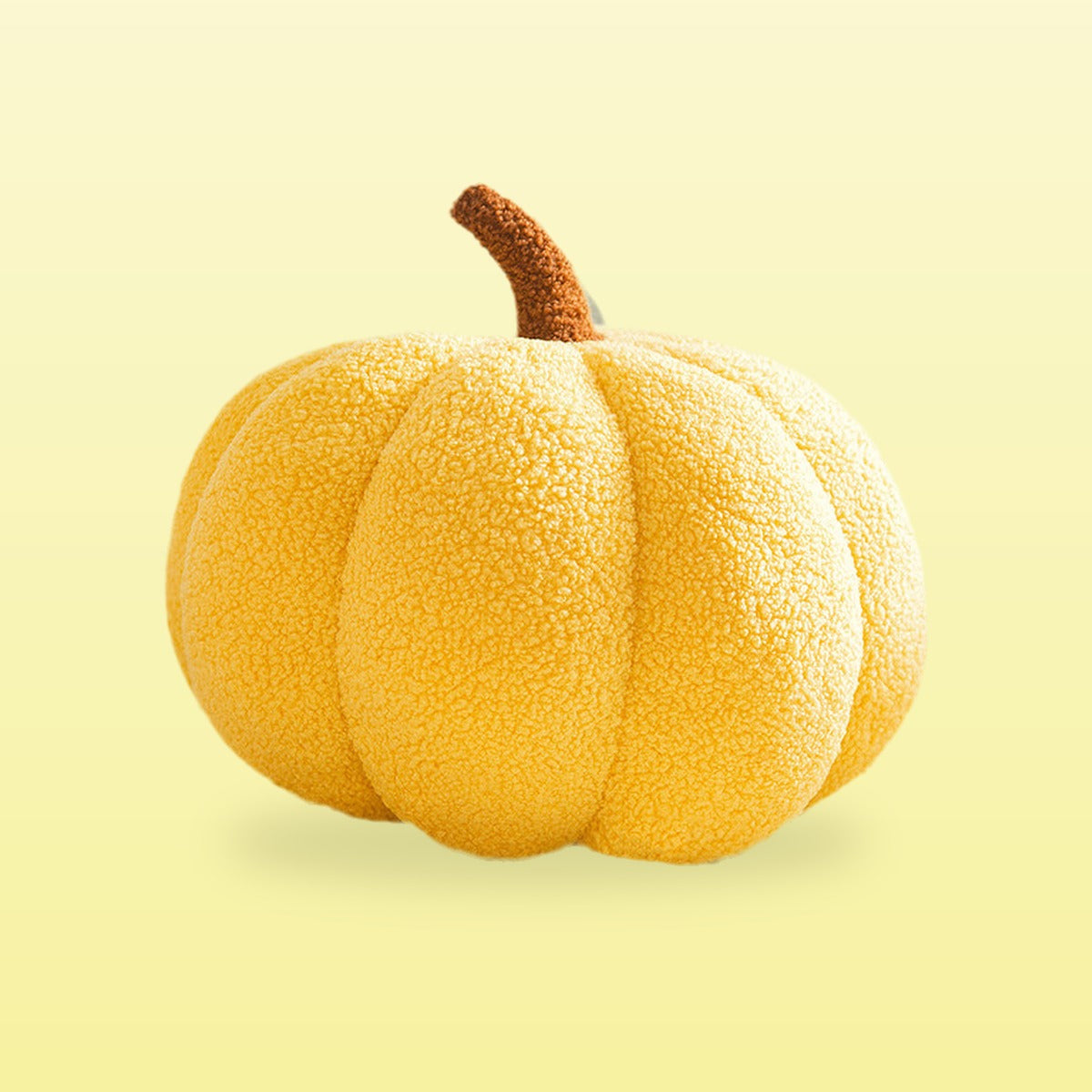 Teddy pumpkin plush cushion, sunflower yellow with a brown stem, on a butter yellow background