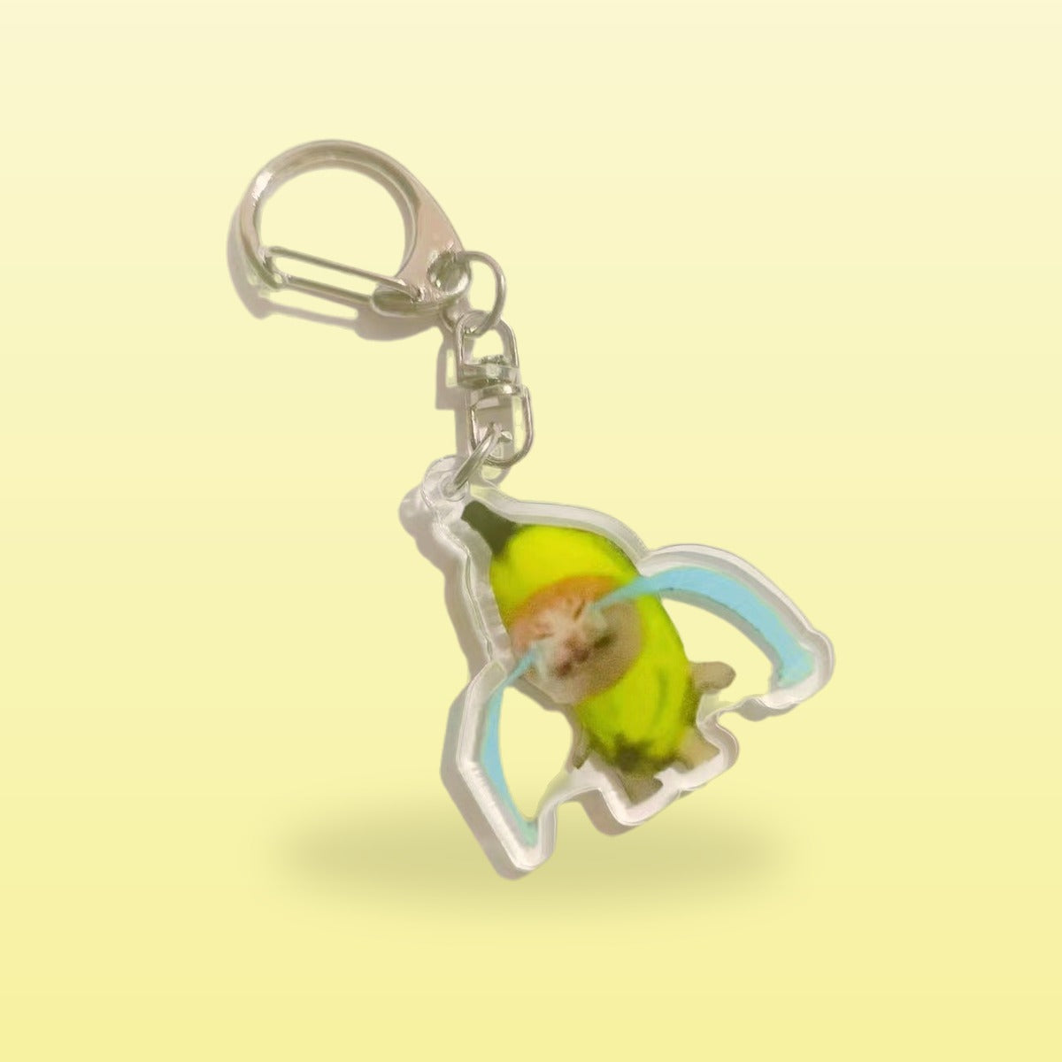 Crying banana cat meme acrylic keychain with a silver clip, on a butter yellow background