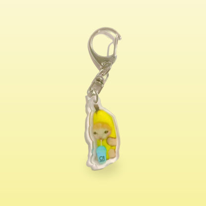 Banana cat meme acrylic keychain holding a blue drink with a silver clip, on a butter yellow background