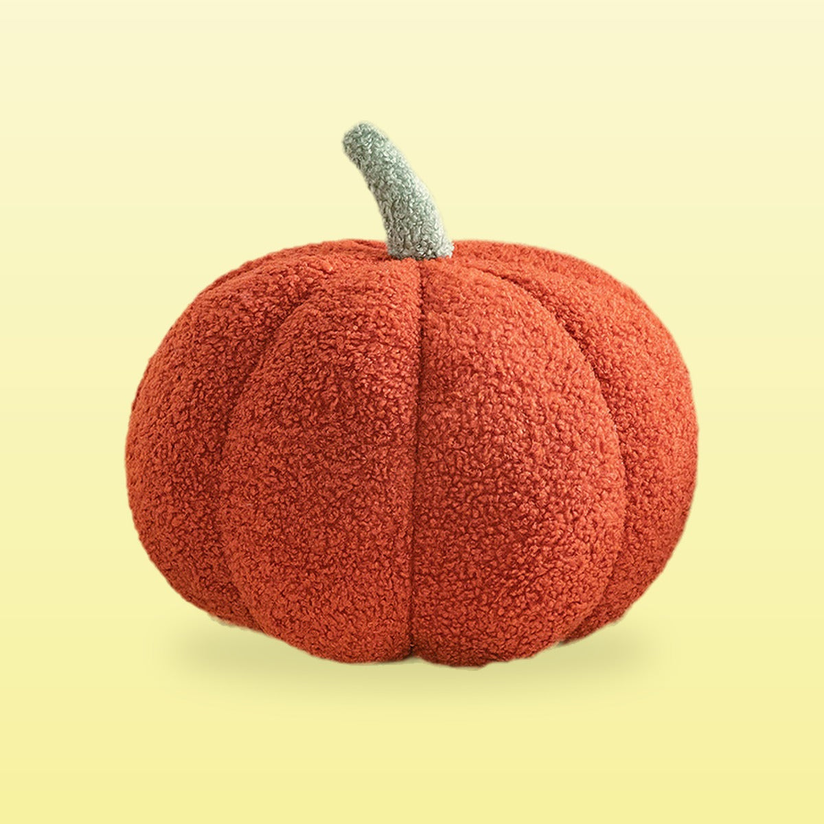 Teddy pumpkin plush cushion, rust red with a sage stem, on a butter yellow background