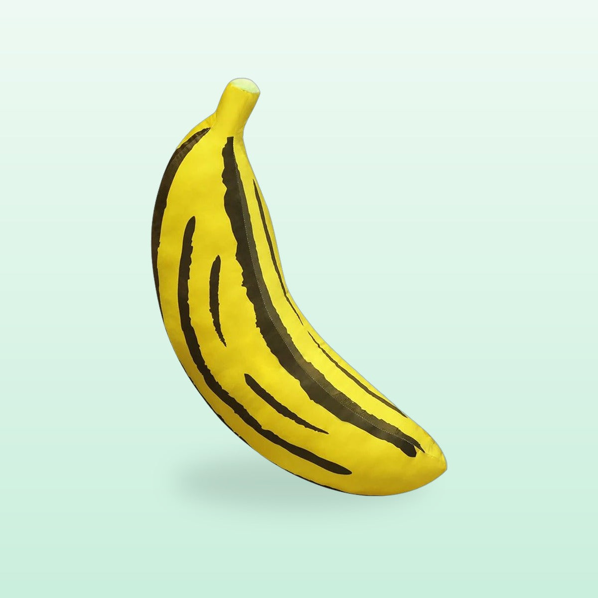 Giant banana plush cushion in yellow with dark stripes, on a mint green background