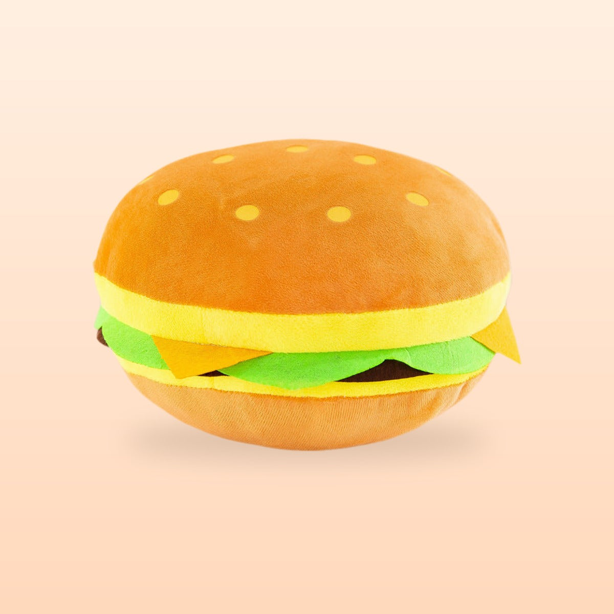 Hamburger plush pillow with an orange bun, cheese and lettuce, on a peach background