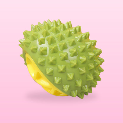 Green durian squeaky dog chew toy with a yellow centre, on a pale pink background