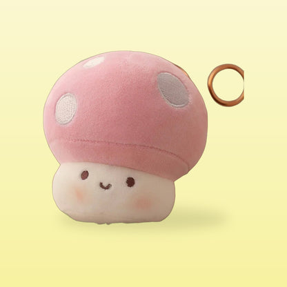 Pink mushroom plush keychain with white spots and a smiling face, on a butter yellow background