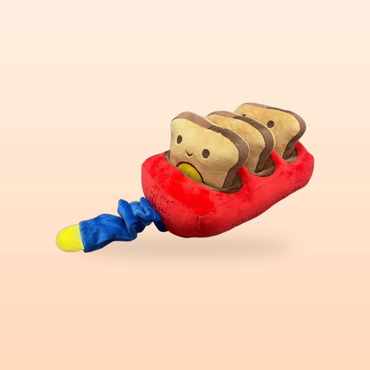 Red bread machine snuffle dog toy with three plush toast slices and a blue pull tail, on a peach background