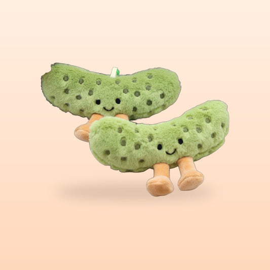 Two pickle plush charms with smiling faces and little legs, on a peach background
