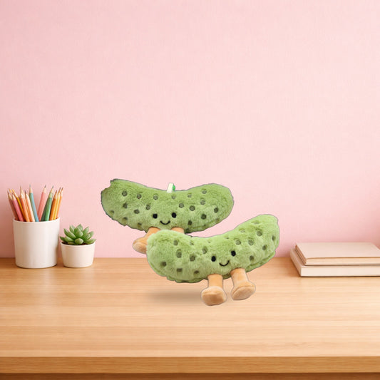 Two pickle plush charms on a light oak desk