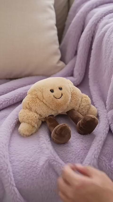 Croissant plush getting a gentle squish on a cosy sofa