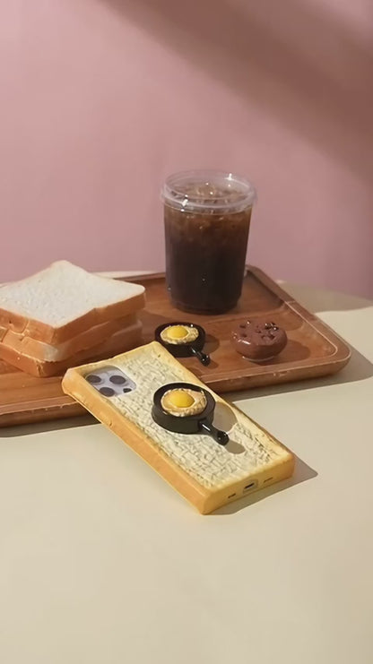 Toast bread iPhone case with the frying pan grip, picked up and turned in a hand on a pastel breakfast table