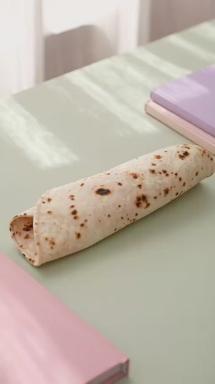Burrito pencil case unrolling on a desk to show the tortilla print and pen strap