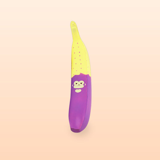 Monkey noodle banana squishy charm, yellow with pink dots and a purple base, on a peach background