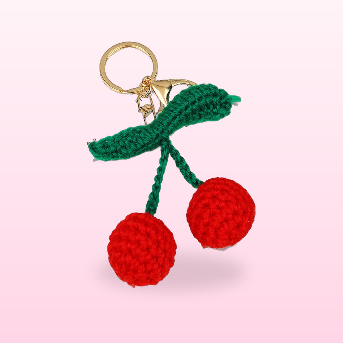 Close up of the crochet cherries keychain with a green leaf and gold clasp