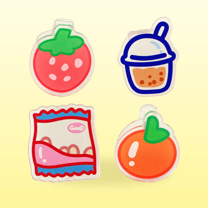 Four acrylic snack page clips: a strawberry, a bubble tea, a packet of chips and a persimmon on a butter yellow background