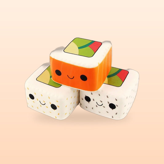 Orange, sesame and black sesame maki roll squishy toys stacked together, on a peach background
